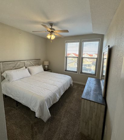 Bright bedroom in rental apartment with queen bed, ceiling fan, and large window.