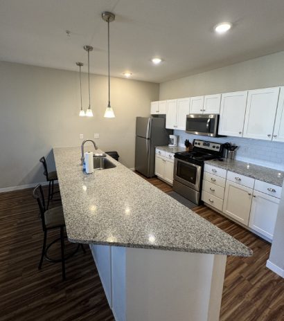 Open-concept kitchen with granite countertops, white cabinetry, and stainless steel appliances.